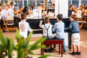 In Plovdiv, four young boys playfully gather around a black grand piano during an evening wedding reception, their laughter and curious energy adding a touch of youthful charm and levity to the elegant celebration setting.